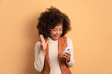 excited brazilian woman checking smartphone  in beige colors. app, social media, connection...