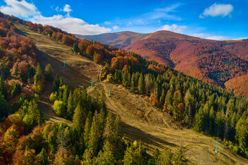 Aerial view of mountains at sunrise in autumn in Ukraine. Colorful landscape with mountain road, forest, houses on the hills, sunlight, sky in fall.