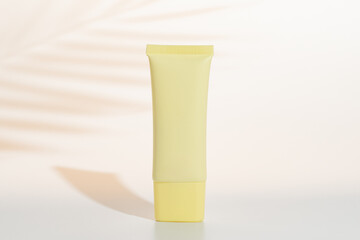 Mockup of yellow tube of body cream with palm shadows at the background, hard lihgt