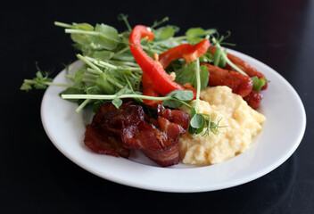 Breakfast in Sweden, Nordic style: bacon, scrambled eggs, red pepper and green vegetables. Delicious and nutritious start for the day on a white plate. Black background.