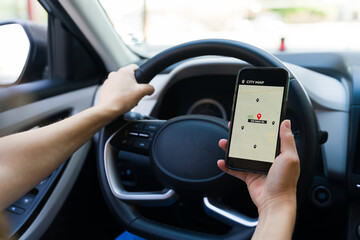 Female driver utilizes a navigation app on her mobile phone to navigate while driving, highlighting...