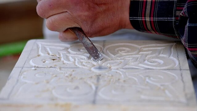 Close-up of an artisan skillfully carving intricate designs on stone in an outdoor setting. Captured in detail.