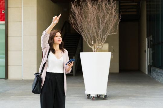 Expectant young woman using smartphone app to hail rideshare pickup while standing outside