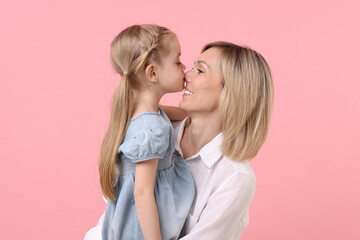 Daughter kissing her happy mother on pink background