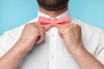 Man in shirt adjusting bow tie on light blue background, closeup