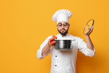 Professional chef smelling something in cooking pot on yellow background, space for text