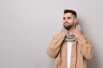 Smiling man in warm scarf on light grey background. Space for text