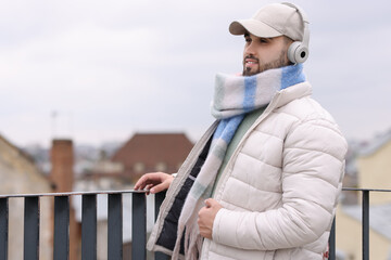 Handsome man in warm scarf and headphones outdoors. Space for text