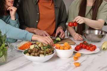 Friends cooking healthy vegetarian meal at white marble table in kitchen, closeup