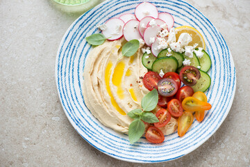 Blue and white plate with hummus and fresh vegetables, horizontal shot on a beige stone background, selective focus