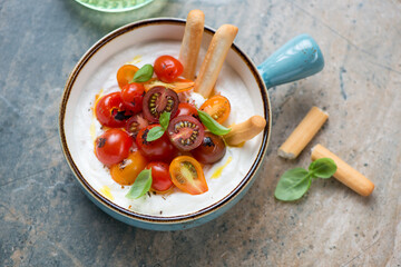 Turquoise serving bowl with ricotta dip and roasted tomatoes, horizontal shot on a grey and beige granite background, elevated view