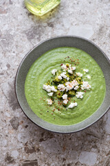 Bowl of broccoli cream-soup topped with feta cheese, vertical shot on a light-brown granite surface, high angle view