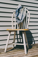 Old and dirty blue jeans draped over wooden chair on patio deck