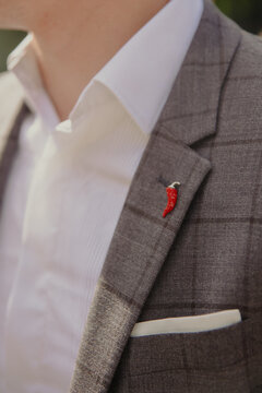 A close-up of a groom wearing a gray checkered suit with a chili-shaped pin on the lapel, adding a playful touch to the formal attire.
