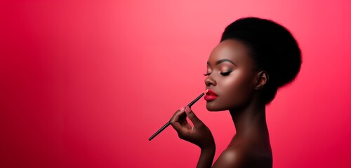 A beautiful black woman with red lip and makeup holding a brush on her mouth, on a bright pink background. with copy space
