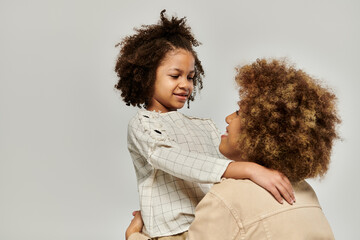A curly African American mother and daughter wearing stylish clothes hug each other affectionately...