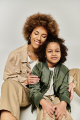 A curly African American mother and daughter, dressed stylishly, posing for the camera against a...