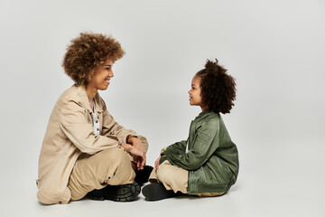 A curly African American mother and daughter sit closely on the floor, sharing a tender moment in...