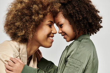 A curly African American mother and daughter, dressed in stylish clothes, share a heartfelt hug...