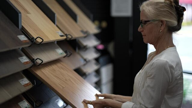 Happy mature woman running hand across solid or engineered wood plank samples in a floor or hardware store for a home remodeling renovation redecorating project.