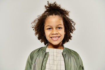 A curly African American kid in stylish clothes wearing a green bomber jacket.