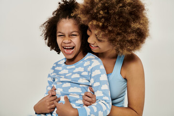 Happy African American mother and daughter in pajamas sharing a joyful moment, laughing together on...