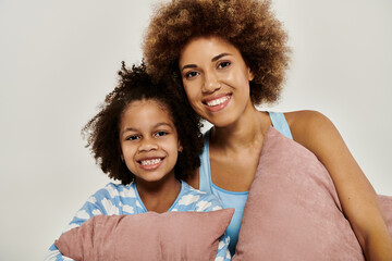 Happy African American mother and daughter smiling in pajamas while posing together on a grey...