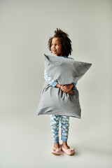 A little girl in pajamas cuddling a grey pillow. Cozy vibes ensue.