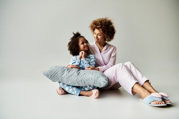 An African American mother and daughter sitting on the floor in pajamas, sharing a warm and joyful...