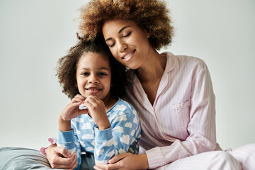 Happy African American mother and daughter in pajamas, sharing a tender moment on a cozy bed...