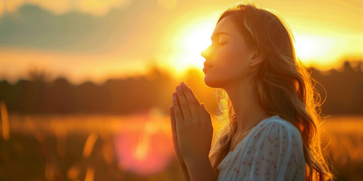 Young lady praying with the sun setting behind her.