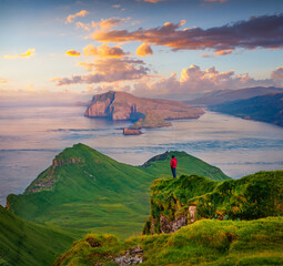 Tourist in red jacket admiring of sunset on Alaberg cliffs, Faroe Islands, Denmark, Europe. Aerial...