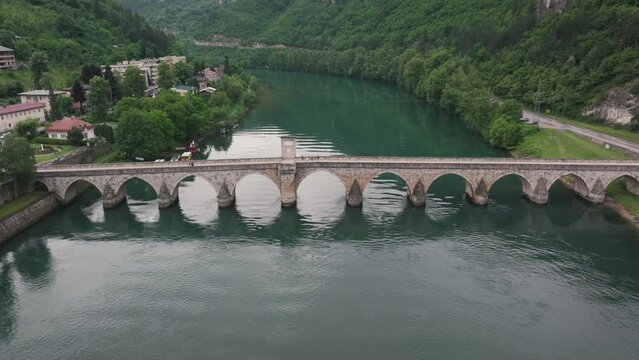 Drone footage of Mehmed Pasa Sokolovic Bridge over the emerald-green Drina River in Visegrad, Republika Srpska. Aerial view highlights the 16th-century Ottoman design and surrounding natural beauty.