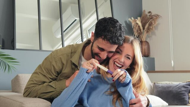 Caucasian couple holding a pregnancy test and looking at camera with a happiness expresion. Husband and wife checking the result of the maternity exam and smiling for their new baby. Parenthood