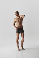 Young, fit male model with platinum blonde hair poses confidently, showing defined physique isolated on grey studio background. Concept of male beauty, body care, fitness, sport, health