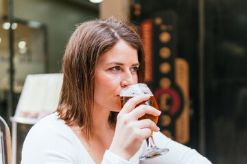 Young woman savors a refreshing beer while seated outdoors at a casual dining venue