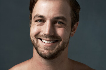 Naklejka premium Man, portrait and smile for skincare in studio, confidence and beauty on blue background, Male person, happy and cosmetics for facial treatment or clean and smooth skin, dermatology and proud health