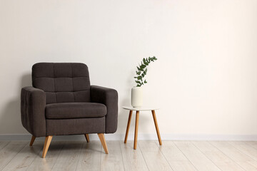 Comfortable armchair, side table and eucalyptus near white wall indoors, space for text