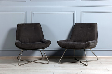 Comfortable armchairs near grey wall in room