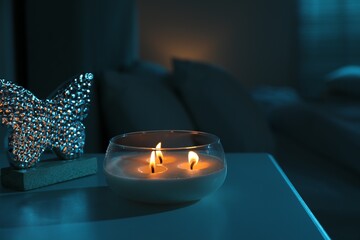 Burning scented candle on bedside table in bedroom at night