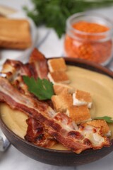 Delicious lentil soup with bacon and parsley in bowl on table, closeup