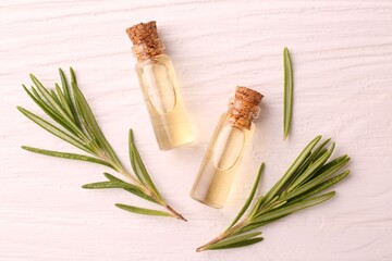 Essential oil in bottles and rosemary on white wooden table, flat lay