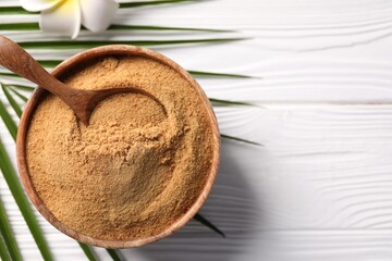 Coconut sugar and spoon in bowl on white wooden table, flat lay. Space for text