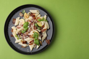 Tasty pasta with bacon and basil on light green table, top view. Space for text