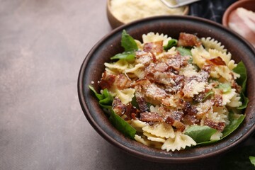 Tasty pasta with bacon and basil on brown table, space for text
