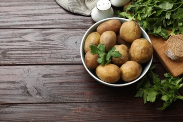 Boiled young potatoes in bowl, parsley and bread on wooden table, top view. Space for text
