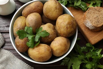 Boiled young potatoes in bowl, parsley and bread on wooden table, top view