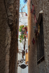 narrow alley between two buildings in a village with decorative objects, revealing the terrace of a house with pots and plants.
