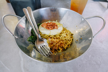 Spicy Indomie fried noodles topped with ground beef and delicious sunny side up egg served on a stainless steel plate with a spoon and fork