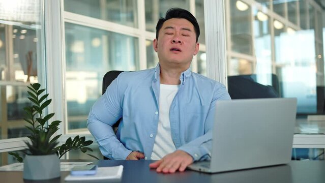 Portrait of regrettable man feeling inflammation of appendix during work process at personal laptop in office environment. Unhappy korean entrepreneur need medical help indoors. Concept of pain.
